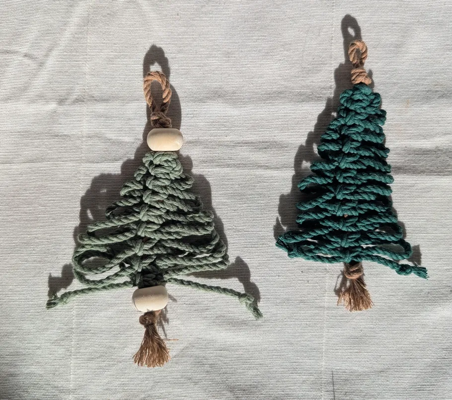 Two macramé tree ornaments on fabric background.