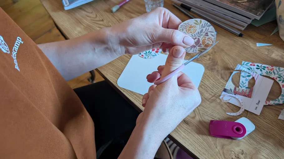 Person schneidet floral gemusterten Papierkreis am Tisch.