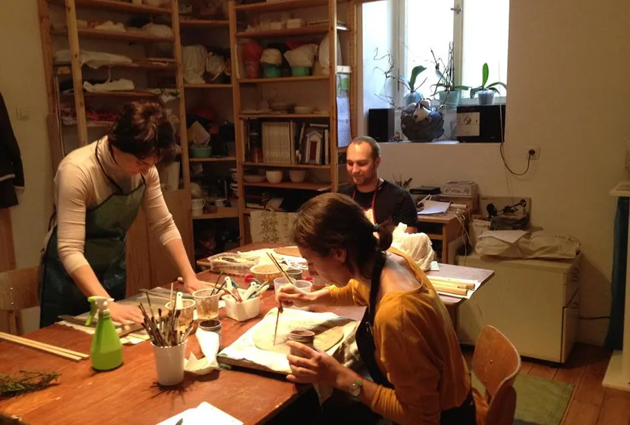 Three people painting around a wooden table.
