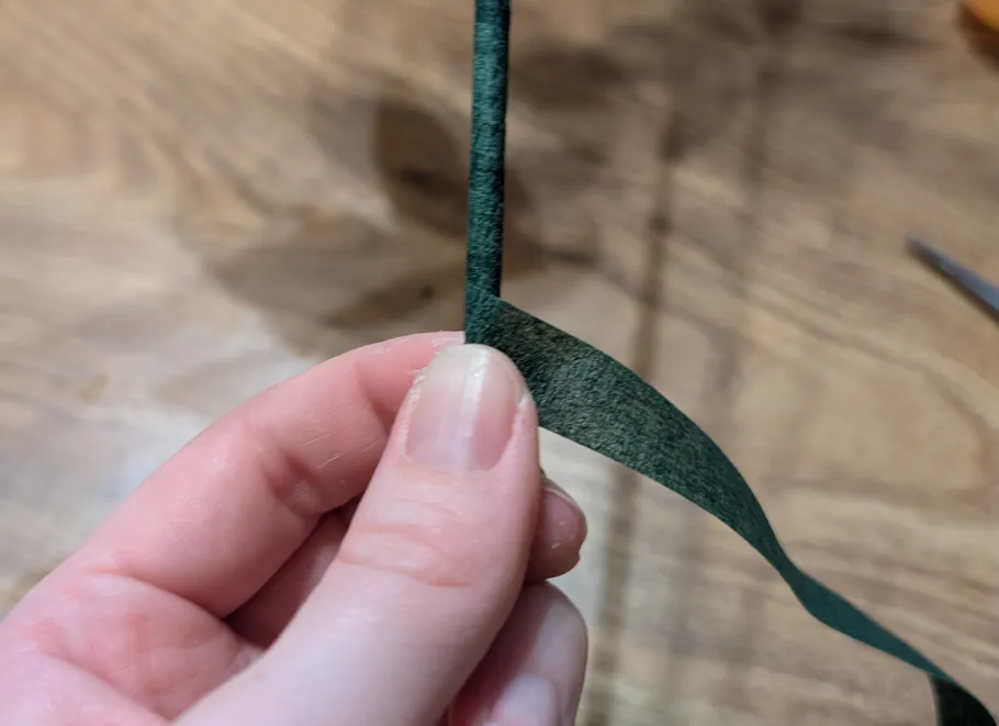 Hand holding green floral tape on wood table.