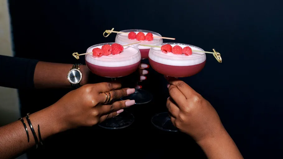 Three hands holding raspberry cocktails.