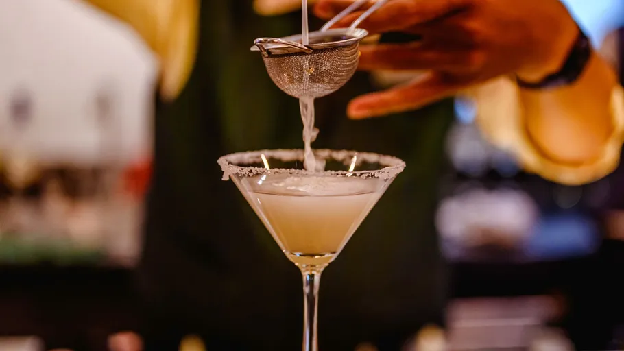 Bartender straining cocktail into martini glass.