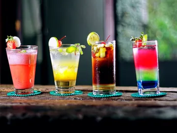 Vier bunte Cocktails stehen auf einem Holztisch.