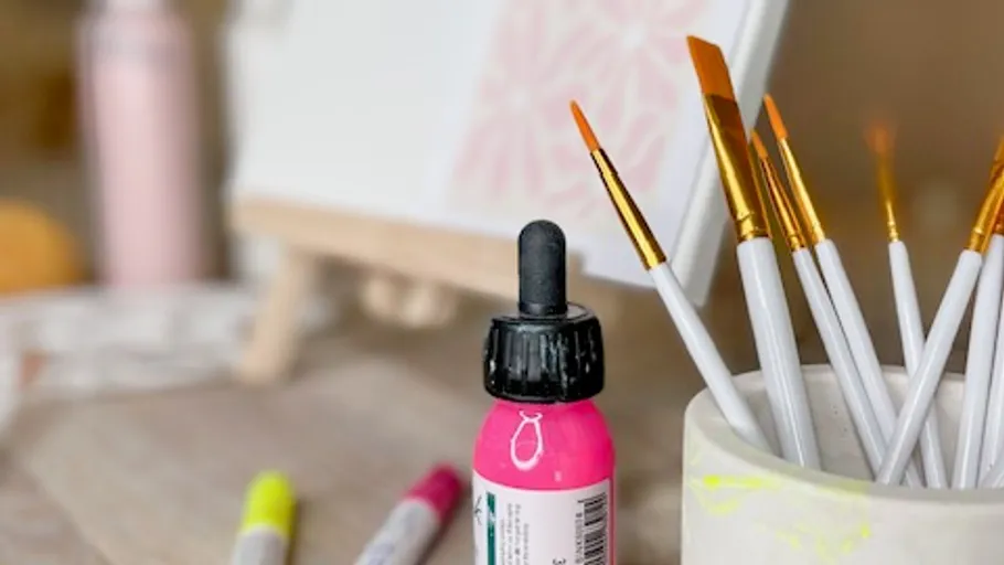 Pinke Farbflasche und Pinsel auf Tisch.