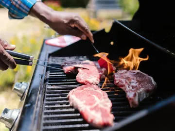 Fleisch wird auf einem Grill gegrillt, Flammen steigen auf.