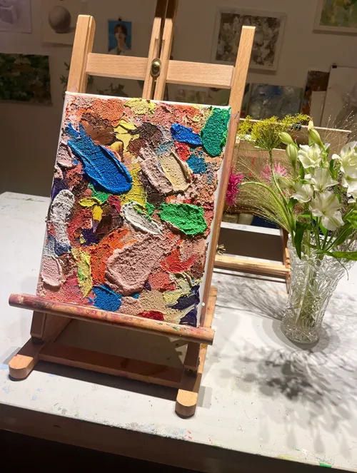 Colorful abstract painting on an easel, vase nearby.
