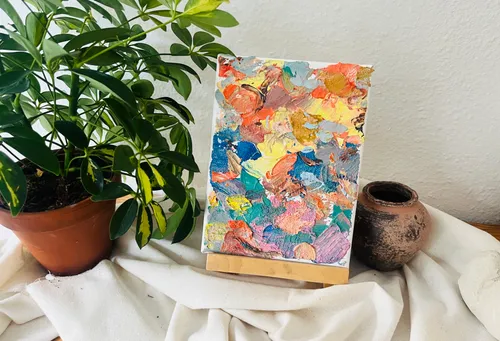 Abstract painting on stand with plant nearby.