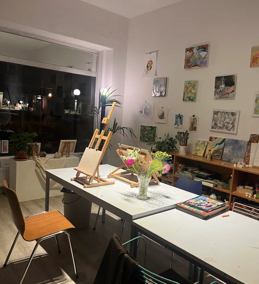 Kunststudio mit Tischen, Staffeleien und Gemälden.