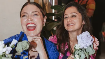 Two women smiling holding flowers indoors.