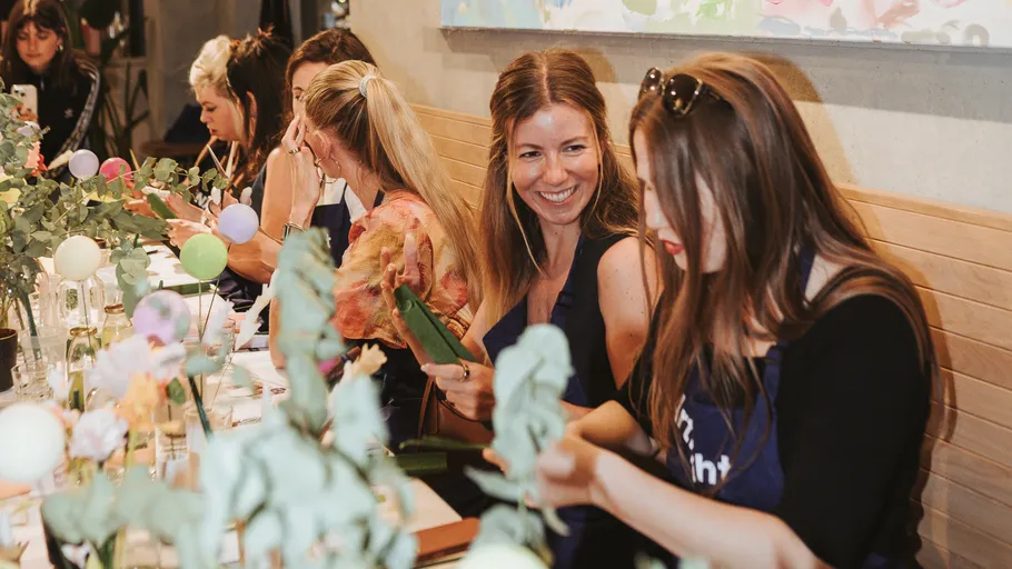 Frauen basteln mit Blumen an einem Tisch.