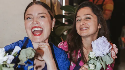 Two women smiling, holding flowers indoors.
