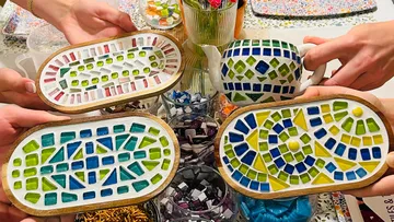 Hände halten bunte Mosaikhandwerke auf Tisch.