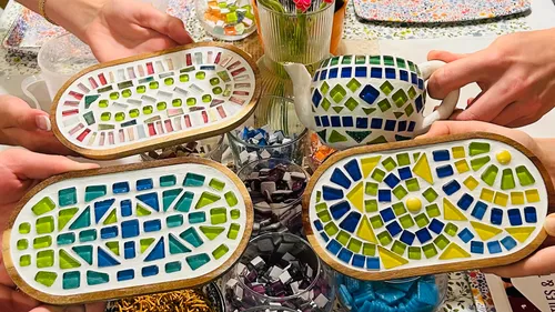 Hands holding colorful mosaic crafts on table.