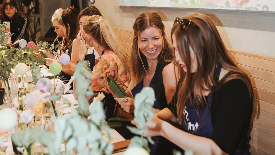 Frauen basteln mit Blumen an einem Tisch.