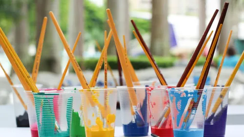 Paintbrushes in colorful paint cups outdoors.