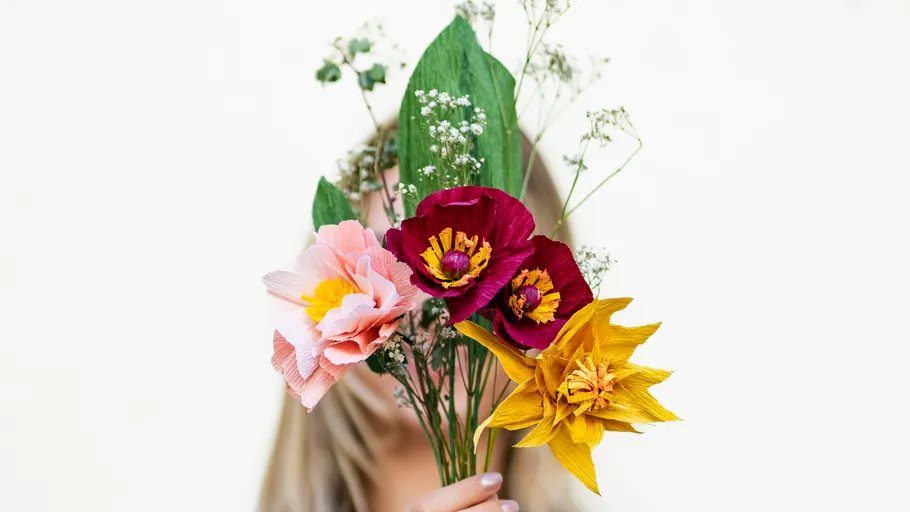 Person hält bunten Blumenstrauß vor weißem Hintergrund.