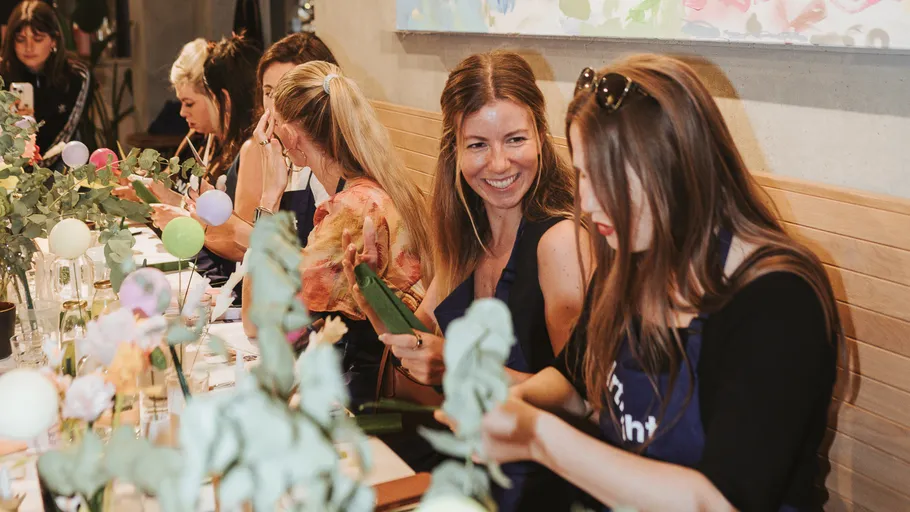 Frauen basteln mit Blumen an einem Tisch.
