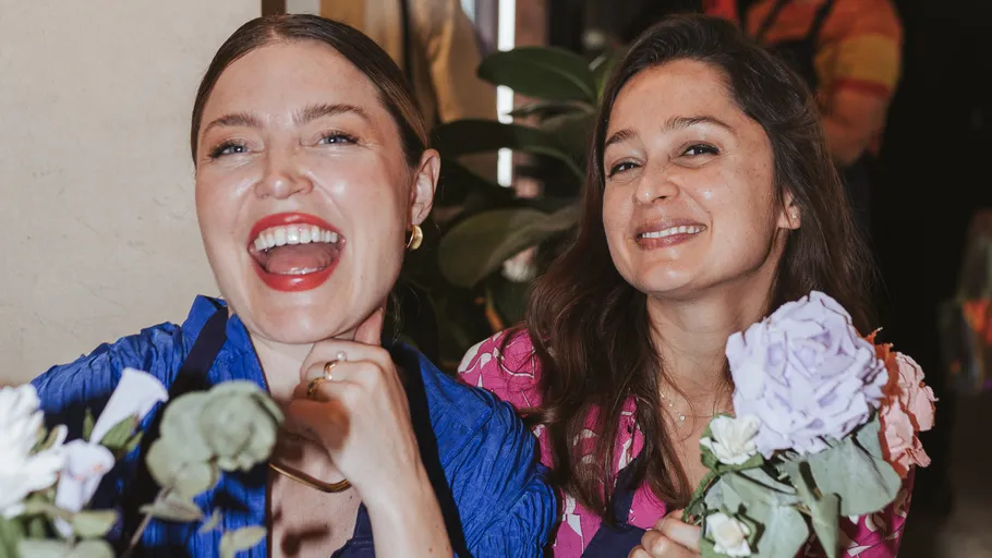 Two women smiling holding flowers indoors.