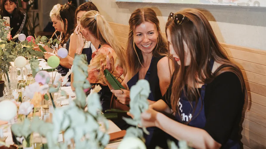Frauen arrangieren Blumen an einem Workshop-Tisch.