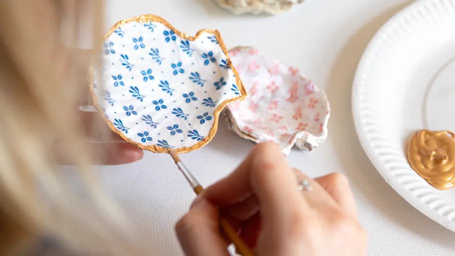 Person painting decorative ceramic piece with gold paint.