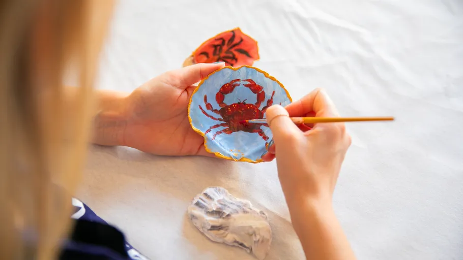 Person painting crab on blue seashell.