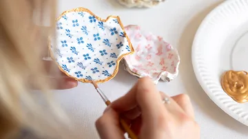 Person painting gold edge on decorative dish.