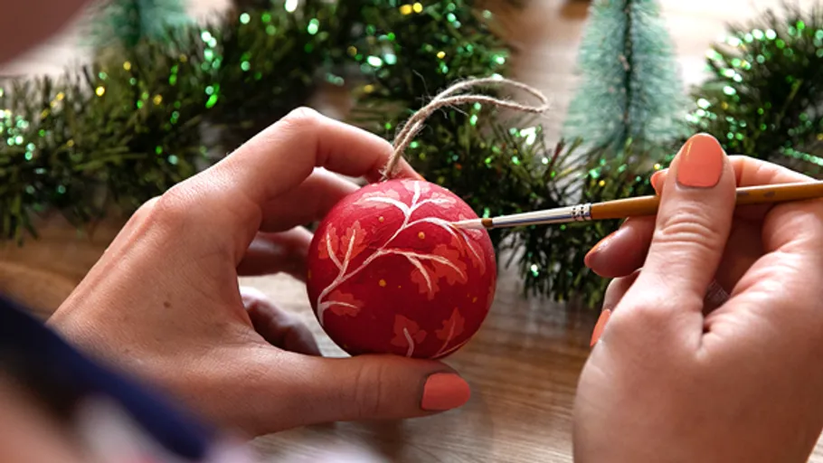 Hände bemalen rote Kugel in festlicher Umgebung.