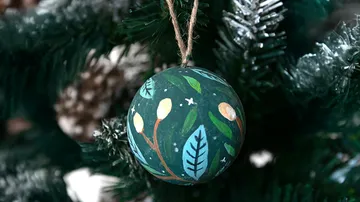 Bemalter Baumschmuck hängt an einem Weihnachtsbaum.