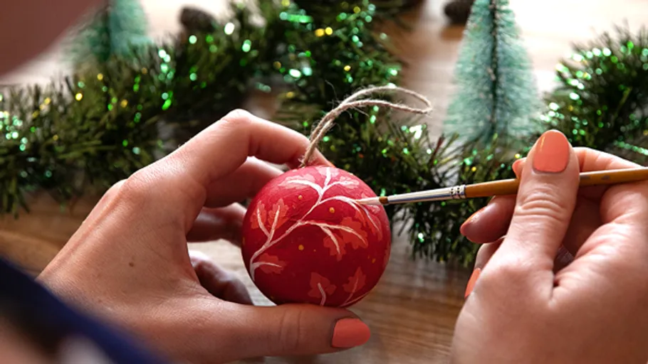 Hände bemalen roten Schmuck auf Holztisch.