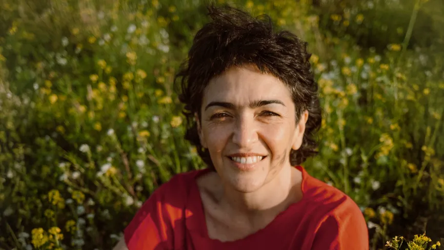 Lächelnde Person im Freien zwischen gelben Blumen.