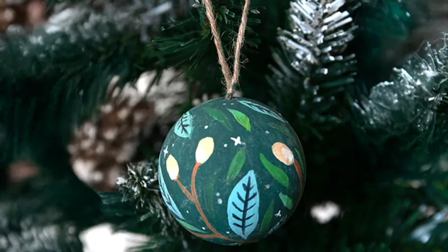 Bemalter Anhänger hängt an Weihnachtsbaum.
