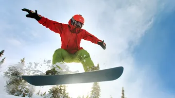 Snowboarder jumps high against clear sky.