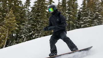Snowboarder fährt verschneiten Hang hinunter, von Bäumen umgeben.
