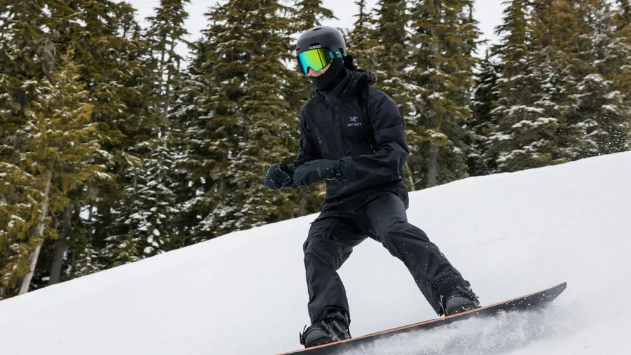Snowboarder descending snowy slope, surrounded by trees.