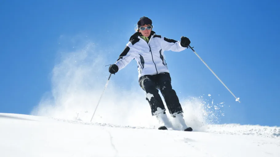 Skifahrer fährt verschneiten Hang unter blauem Himmel hinab.