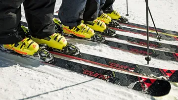 Skiers standing with yellow boots on snow.