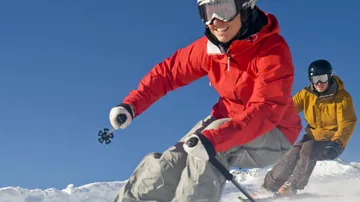 Zwei Skifahrer in bunten Jacken auf schneebedecktem Hang.