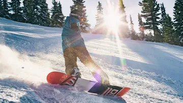 Snowboarder gliding down snowy slope, sunlight shining.