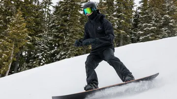 Person snowboardet bergab, umgeben von Bäumen.