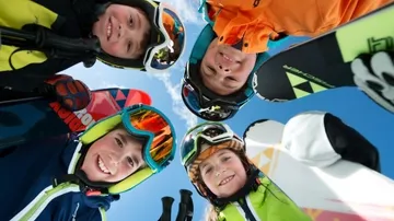 Five skiers smiling, holding skis, blue sky background.