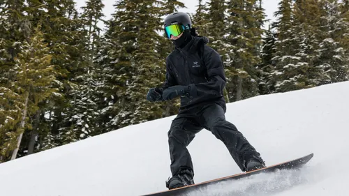 Snowboarder in black gear rides downhill in forest.