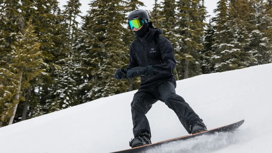 Snowboarder in schwarzer Kleidung fährt im Wald bergab.