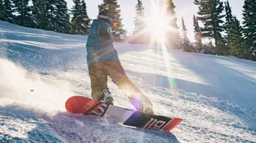 Snowboarder fährt Piste hinunter, Sonne scheint.