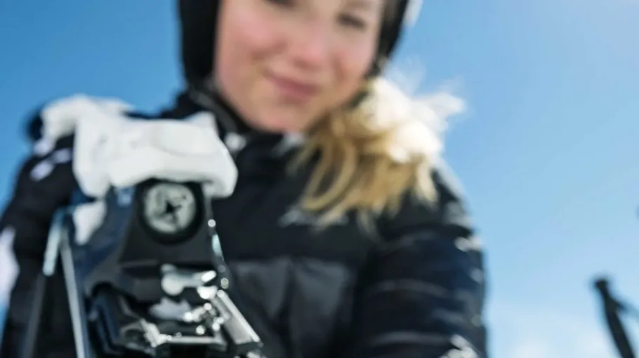 Frau passt Skibindung auf verschneiter Piste an.