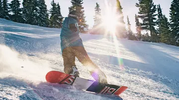Snowboarder gliding down snowy slope with sunlight.