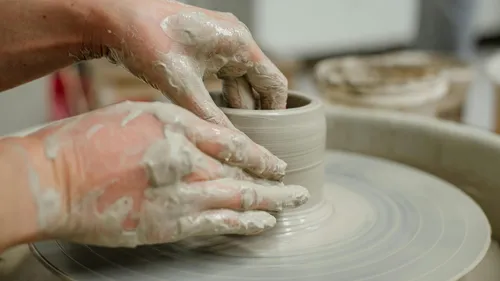 Hände formen Ton auf einer Töpferscheibe.