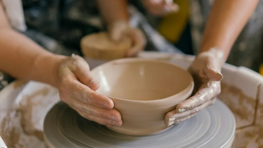 Hands molding clay bowl on pottery wheel.