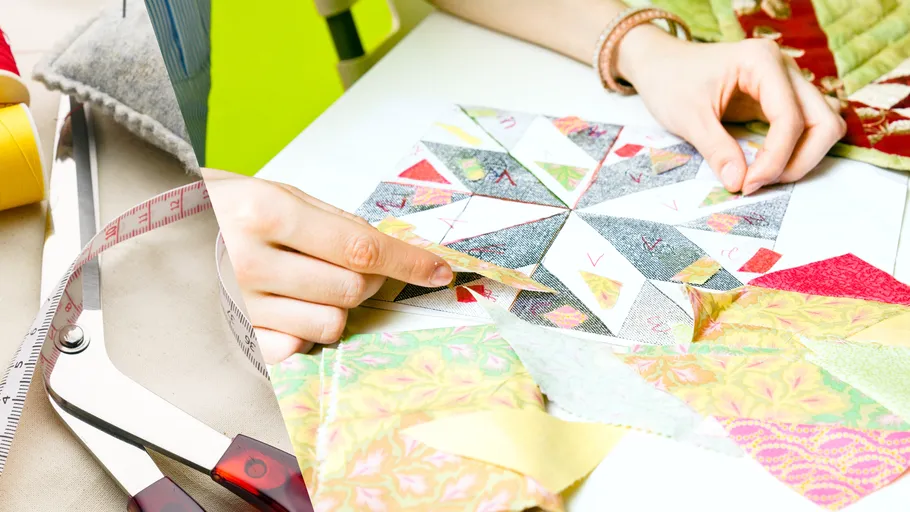 Hands assembling colorful fabric pieces, measuring tape nearby.