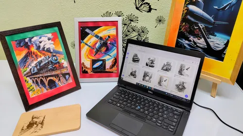 Art frames beside a laptop on a table.