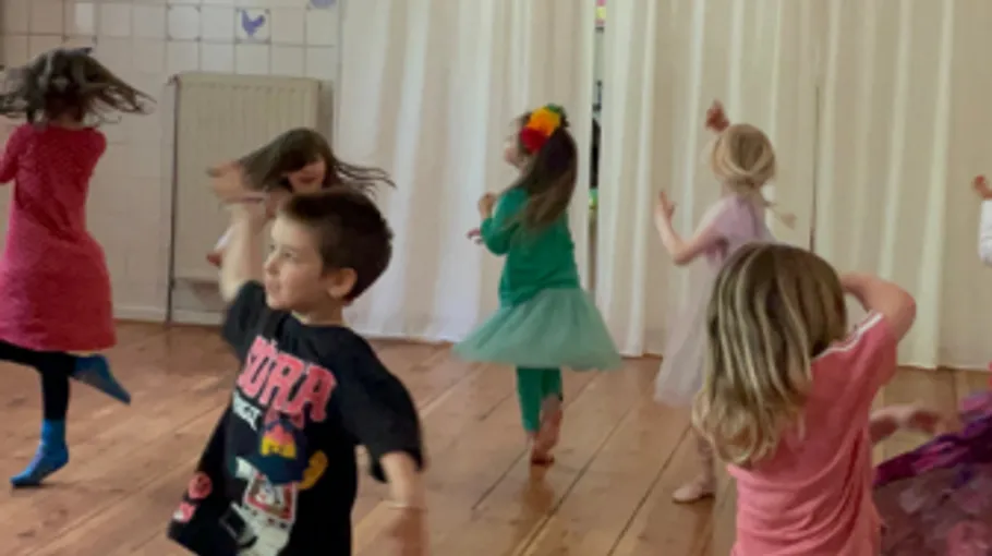 Kinder tanzen auf Holzboden drinnen.